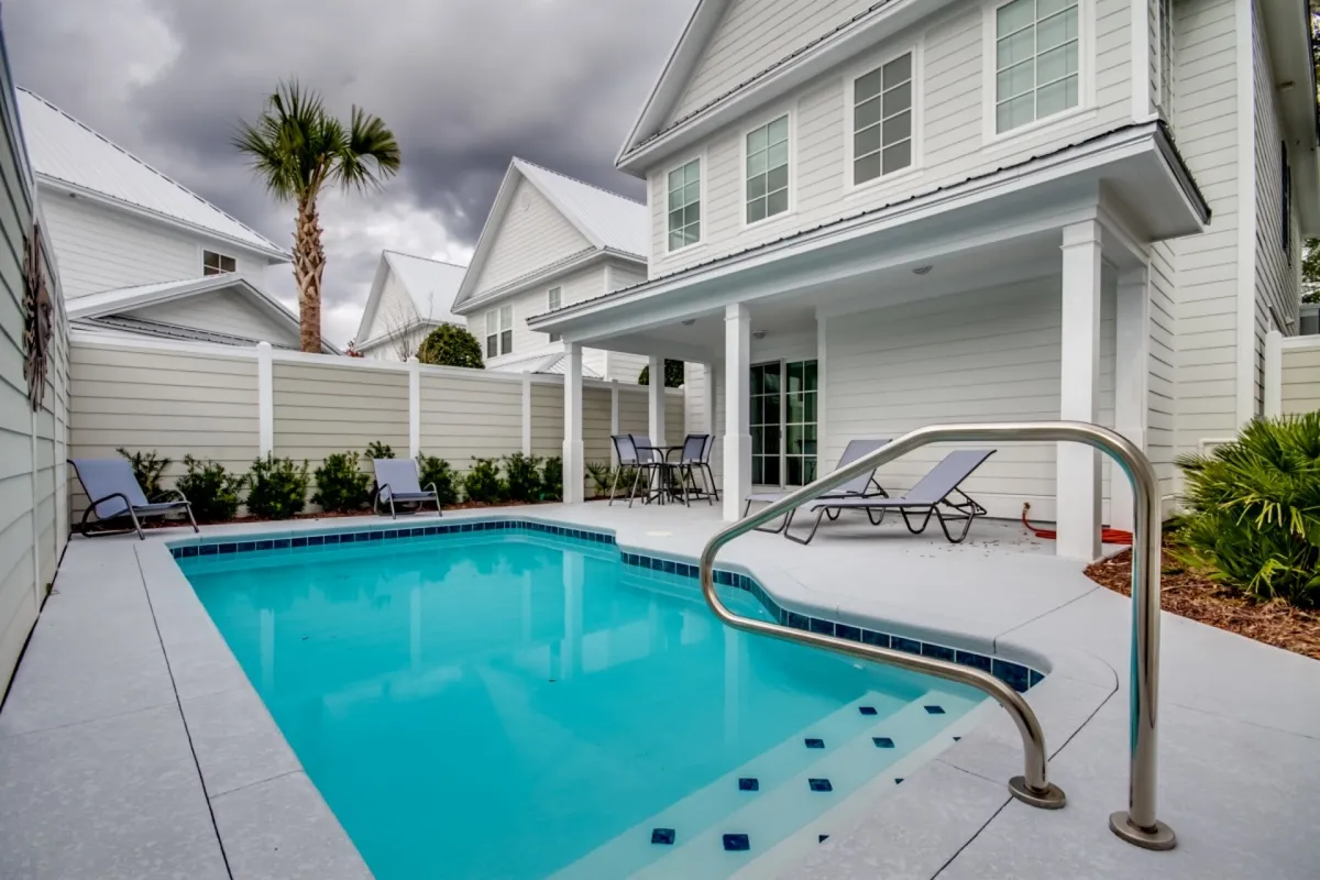 The image showcases the backyard of a single-family house in North Myrtle Beach, featuring a sparkling swimming pool surrounded by comfortable lounge chairs and lush greenery. The tranquil scene invites relaxation and enjoyment, with ample space for swimming, sunbathing, and outdoor gatherings.