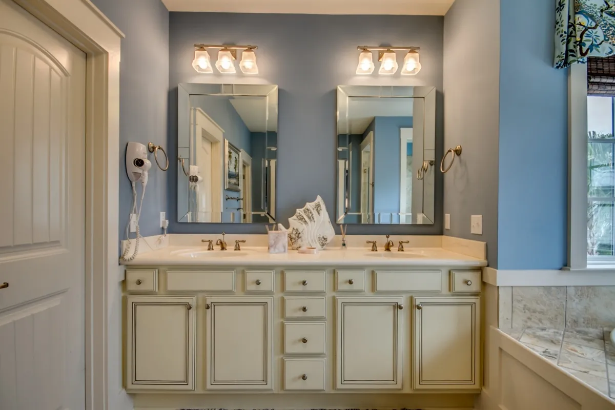 A spa-like bathroom featuring double vanity sinks, large mirrors, and stylish light fixtures. The organized, serene mood is complemented by decorative touches and a calm color palette, creating a sense of relaxation and indulgence.