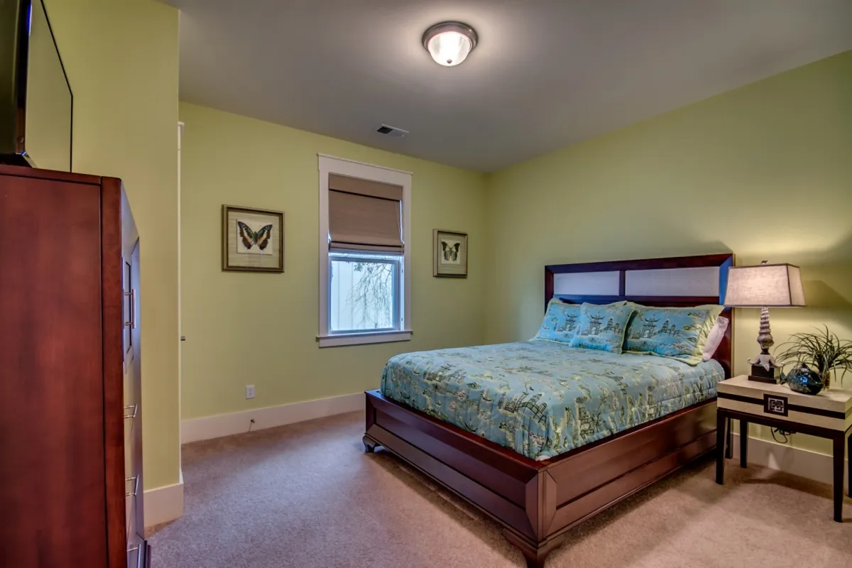 A serene bedroom scene, highlighting a bed with soft, patterned bedding, a warmly lit nightstand, and sunlight streaming through a window. The tranquil atmosphere offers an inviting retreat for rest and rejuvenation.