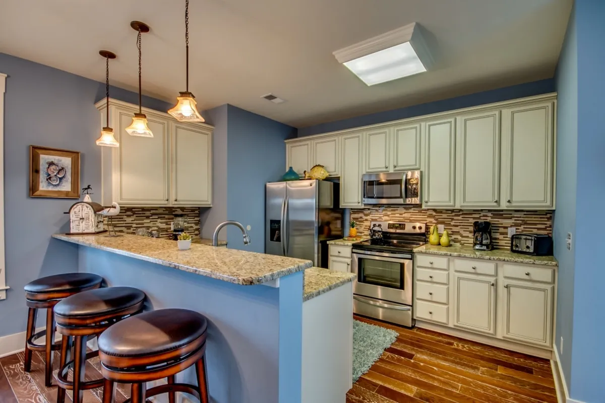 A stylish kitchen scene with a granite countertop, bar stools for casual seating, sleek stainless steel appliances, and elegant backsplash tile. The kitchen is ready for cooking, socializing, and creating shared memories.