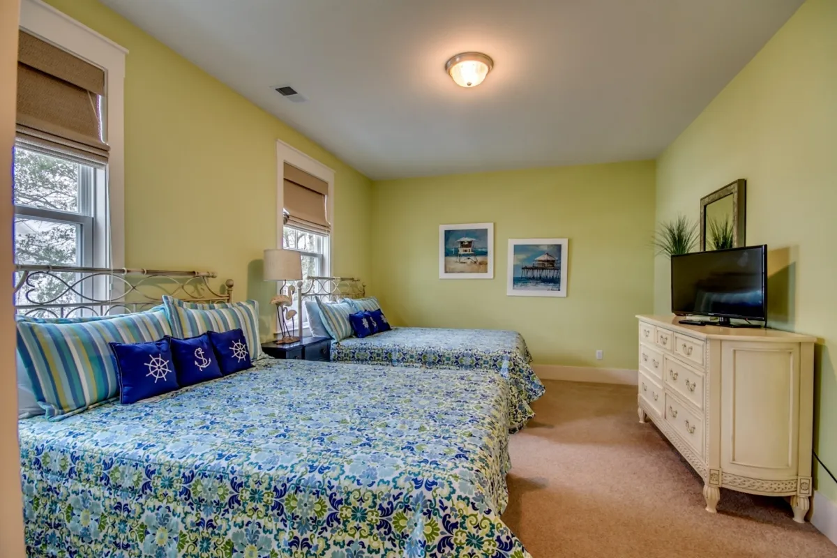 A cheerful bedroom featuring floral bedding, a wall-mounted television, and decorative artwork. The room feels cozy and inviting—perfect for relaxed mornings or winding down at night.