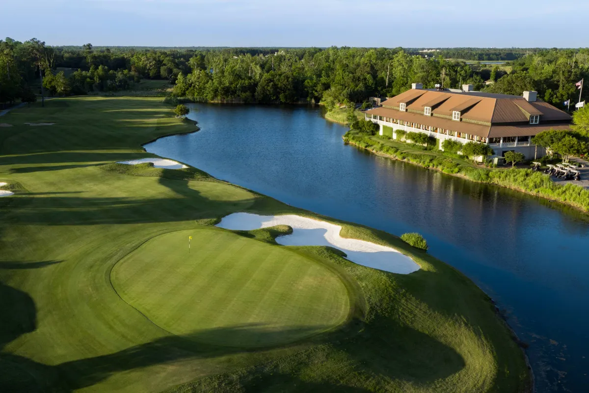 A lush green golf course with a water body, sand traps, and a stately clubhouse in the distance. The setting is open and bathed in gentle sunlight, suggesting a leisurely day playing golf or relaxing outdoors. The landscape is serene yet lively, hinting at available activities and exclusive perks.