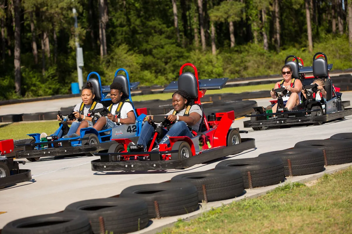 This exterior image captures a group of participants racing go-karts on a winding track surrounded by trees, evoking energy and excitement. The scene is lively, with visible smiles and interaction among racers, highlighting the fun of outdoor activities close to the resort.