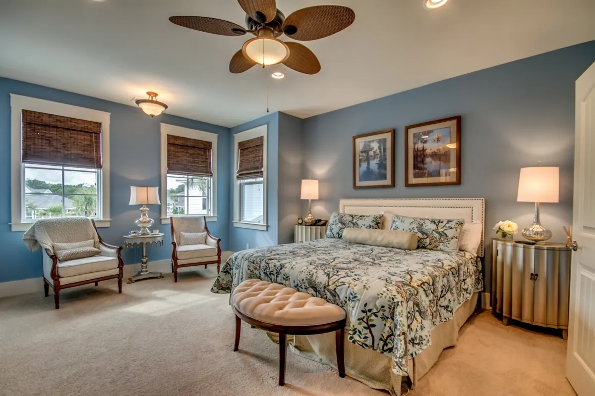 A bedroom with a plush bed featuring decorative bedding, two cozy accent chairs for lounging or reading, a nightstand with a lamp, and a wall adorned with tasteful artwork. Natural light pours into the room, creating a tranquil and inviting atmosphere.