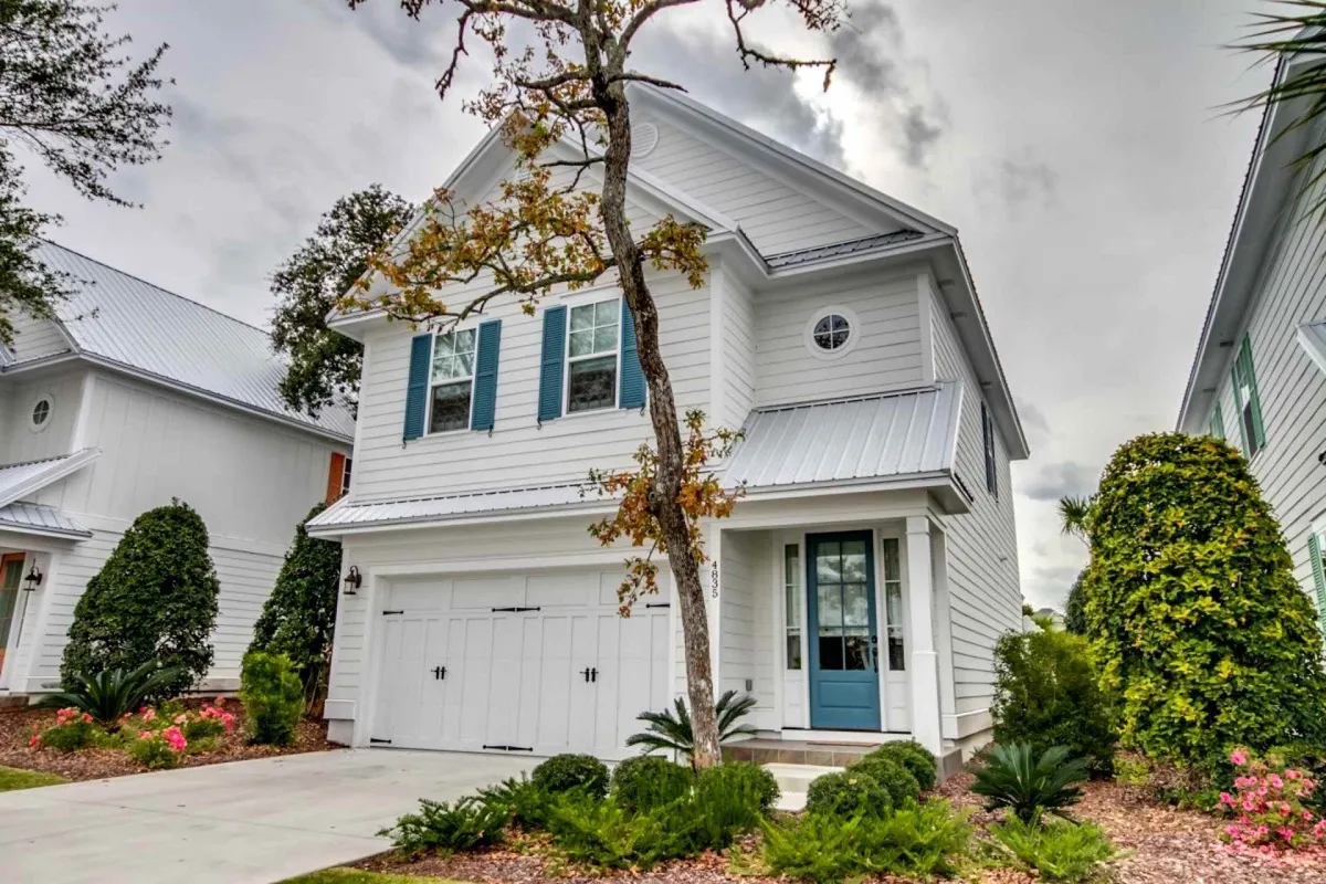 The inviting exterior of the property featuring a white façade, blue shutters, and a covered front porch framed by lush landscaping. Children play in the yard and a family gathers outside, illustrating the home’s potential for outdoor enjoyment and relaxation.